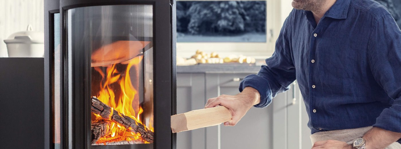 Mann som fyrer i en Jøtul peis